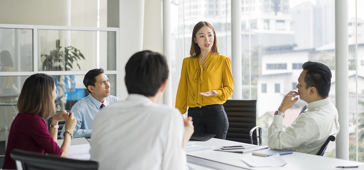 Confident businesswoman giving presentation in board room. Professionals are in meeting at conference table. They are sharing ideas in office.